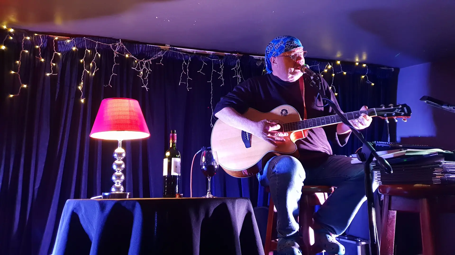 A guitarist on Café Barcelona's stage, under fairy lights and a pink lamp